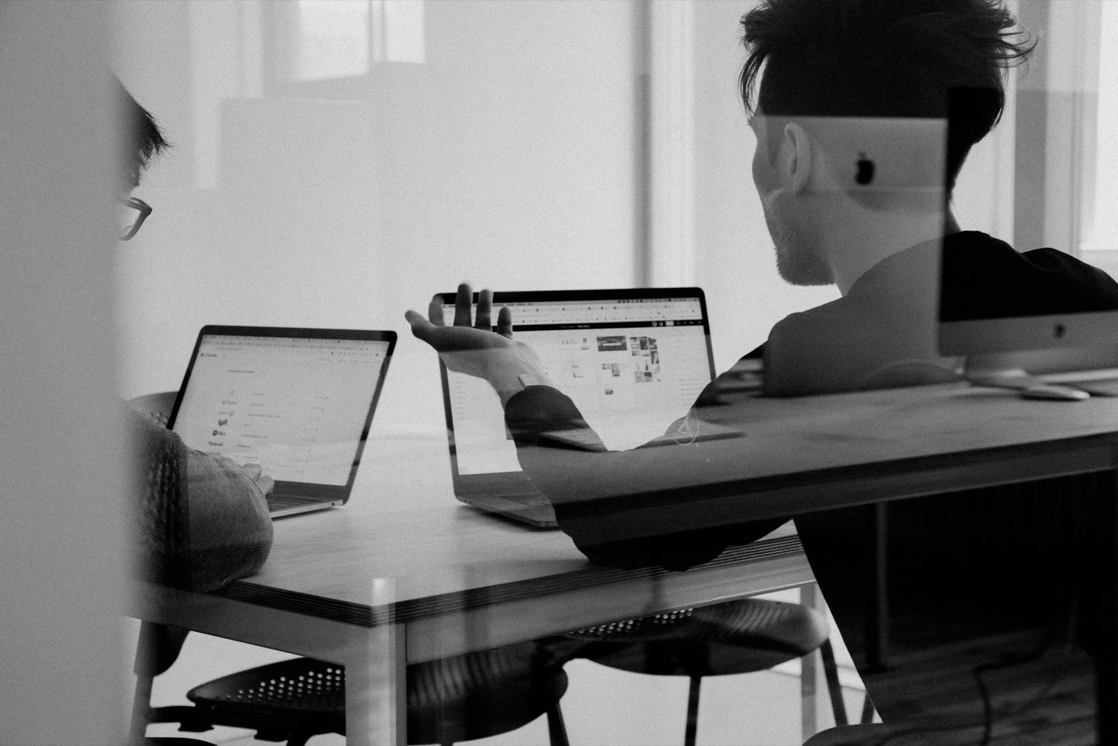 Two people collaborating on laptops at a work table